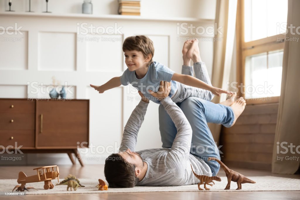 Father and son happily playing with toy dinosaurs in the living room. A heartwarming moment captured in this stock photo.